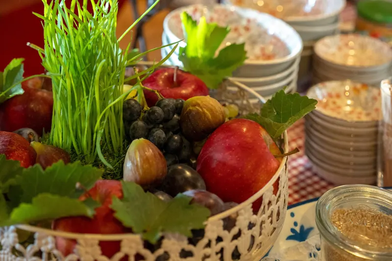 Obstschale mit Äpfeln, Feigen und Trauben, dahinter eine brennende Kerze