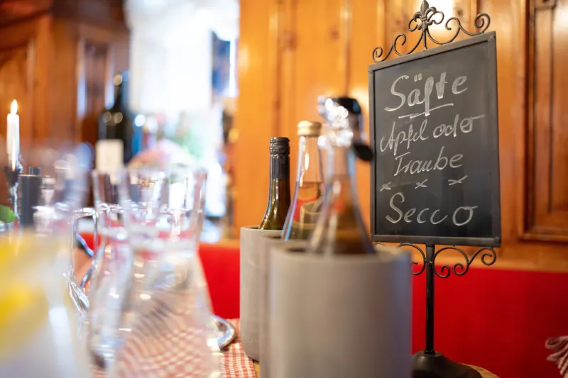 Gläser und Flaschen neben einer Tafel mit der Aufschrift Säfte, Apfel oder Traube, Secco