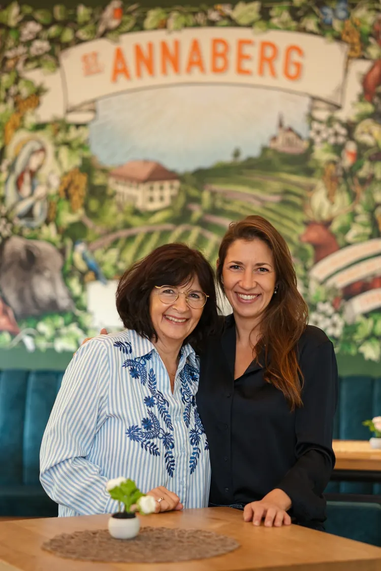 Zwei Frauen stehen lachend in der Weinlounge vor dem Wandbild mit dem Annaberg-Etikett