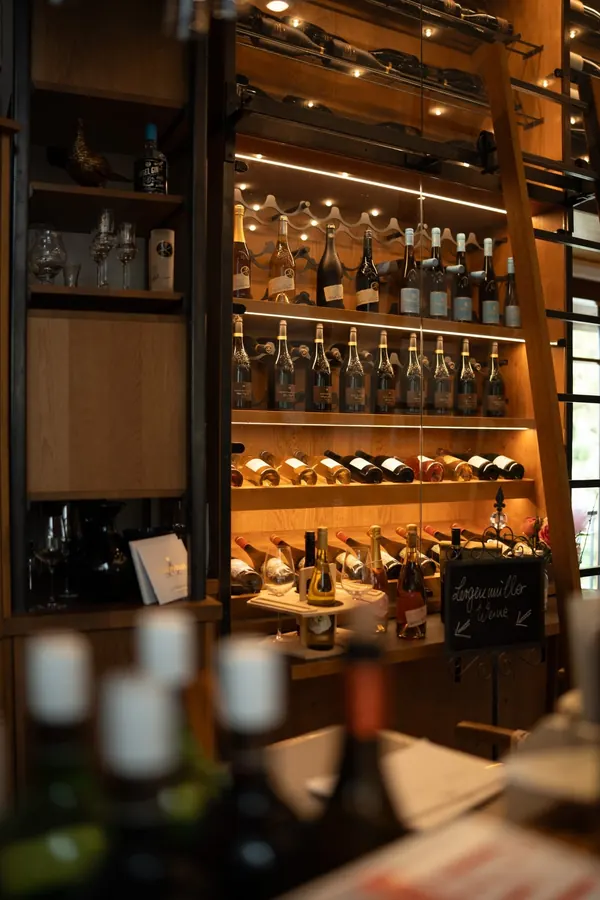 Die beleuchtete Weinwand mit Leiter, im Vordergrund Flaschen auf der Theke
