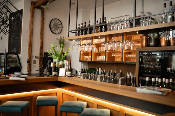 Die Theke der Weinlounge mit Hockern, darüber Gläser und Flaschen im beleuchteten Regal