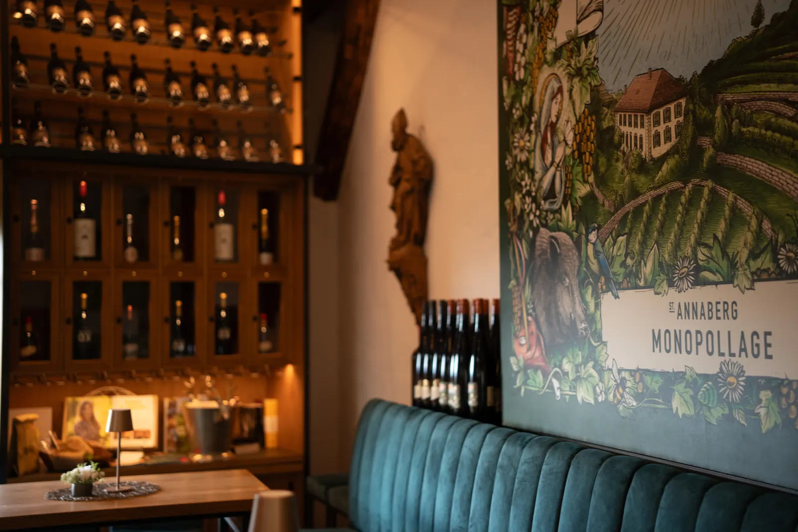 Die Weinlounge 355 NN: beleuchtete Weinwand, grüne Polsterbank und das Etikett als Wandbild mit dem Schriftzug St. Annaberg Monopollage