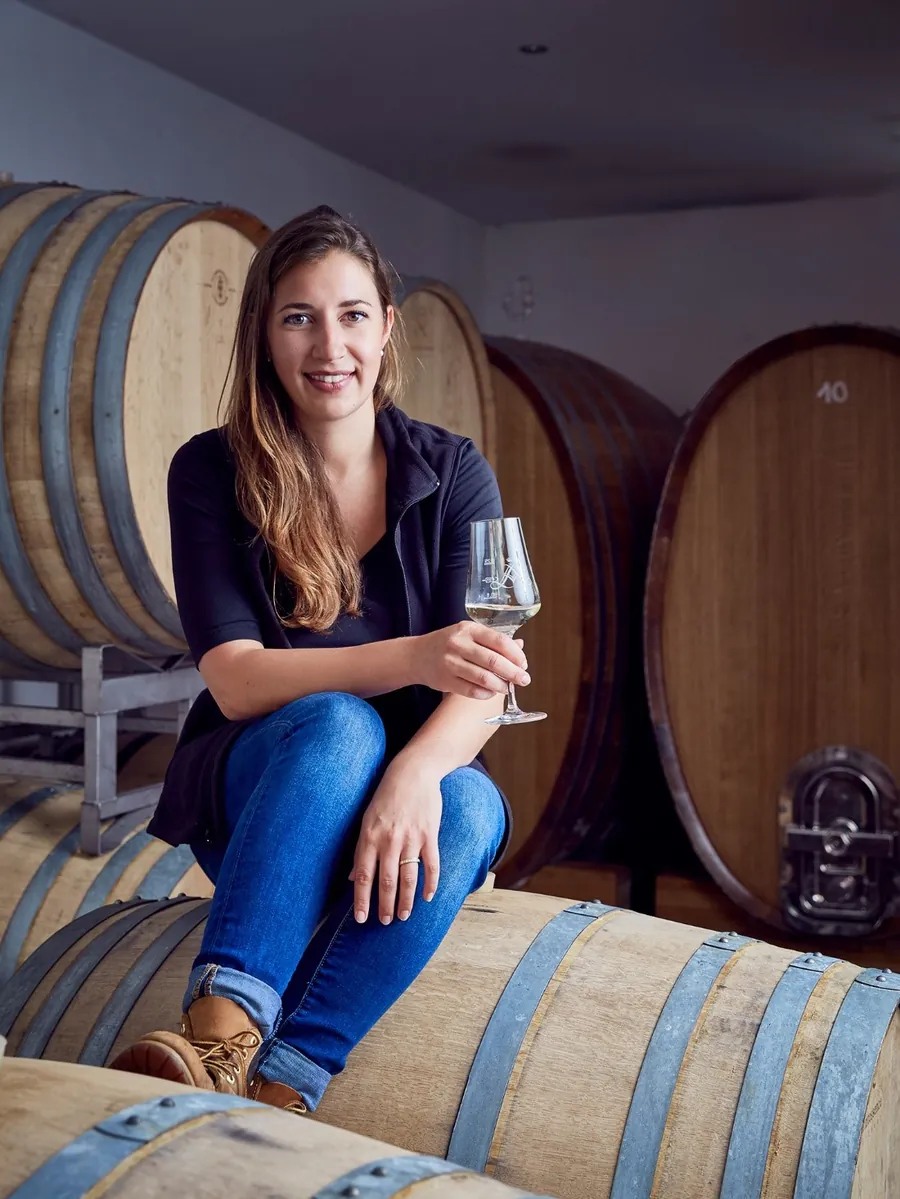 Winzerin Victoria Lergenmüller sitzt mit einem Glas Riesling auf einem Holzfass im Keller
